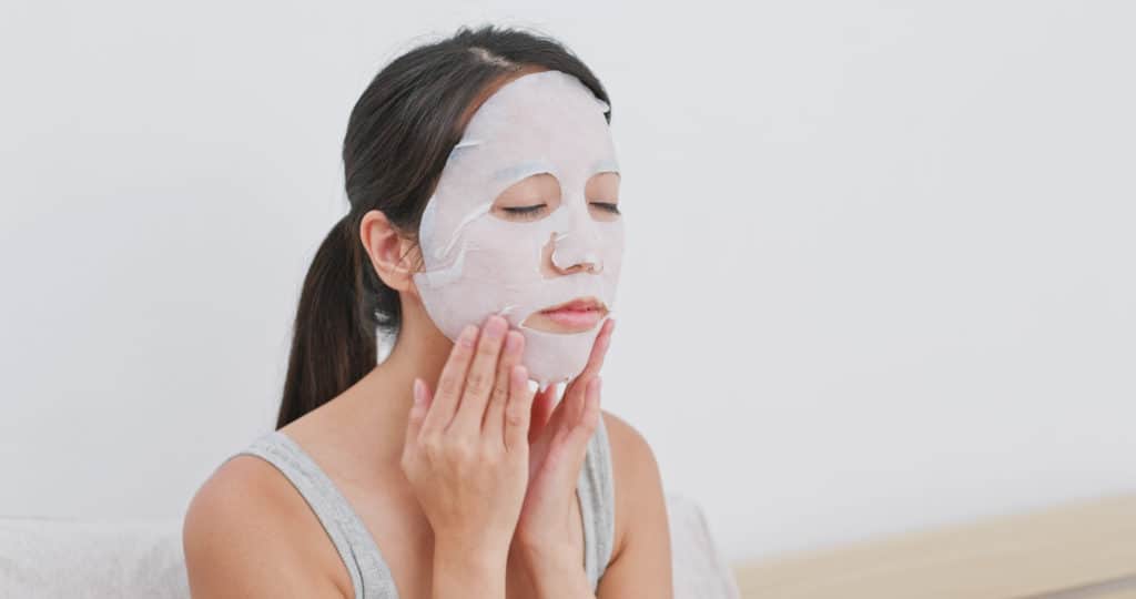 Woman apply facial paper mask on face at home