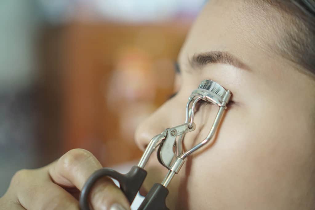 Beauty concept.Close up of woman using eyelash curler while looking in makeup mirror at home.selective focus